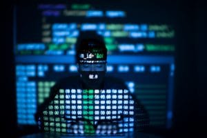 Dieses Bild zeigt einen Mann vor einem Computer, Code ist an die Wand projiziert.