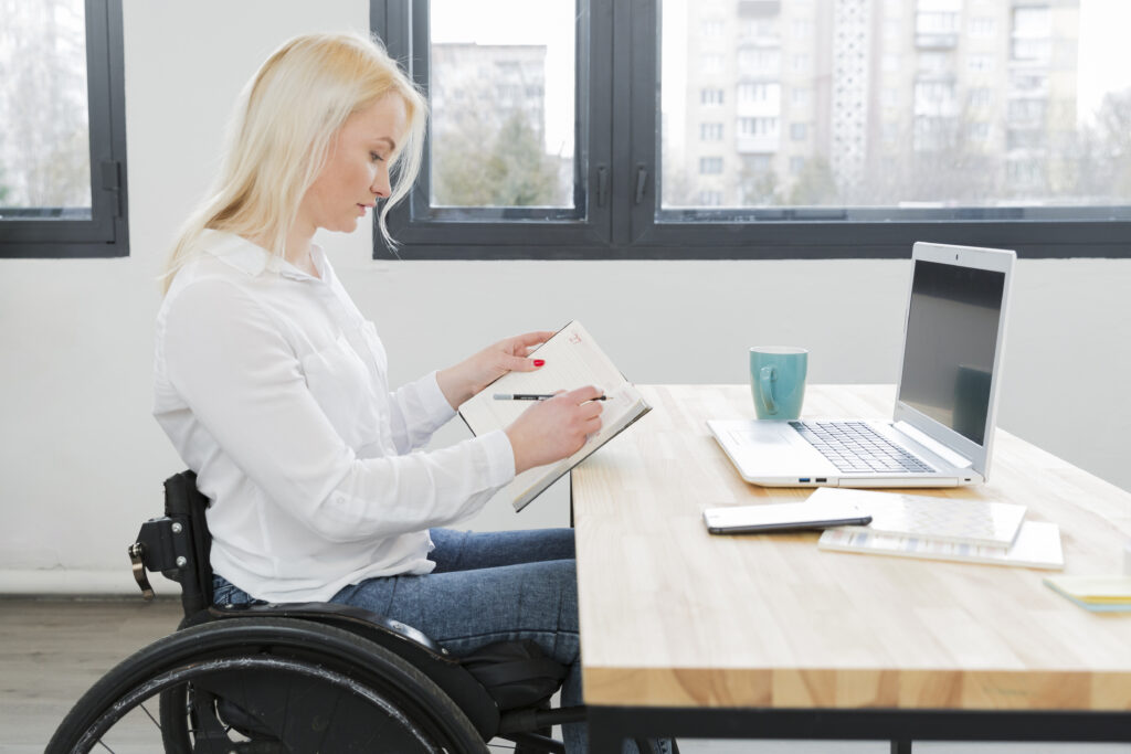 Nainen pyörätuolissa työskentelee kannettavalla tietokoneella
