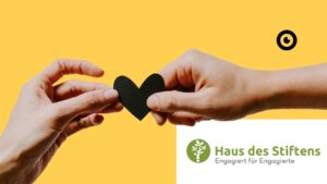 Two hands hold a black heart together. Underneath is the signature: Haus des Stiftens - Engagiert für Engagierte